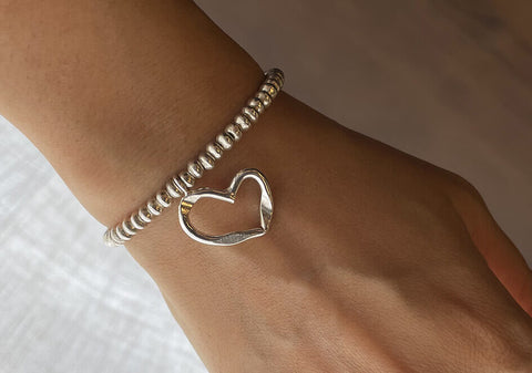A cherished heart beaded bracelet with cut-out heart charm worn on wrist.