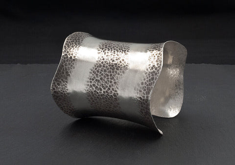 Long curved statement cuff bracelet over a black background