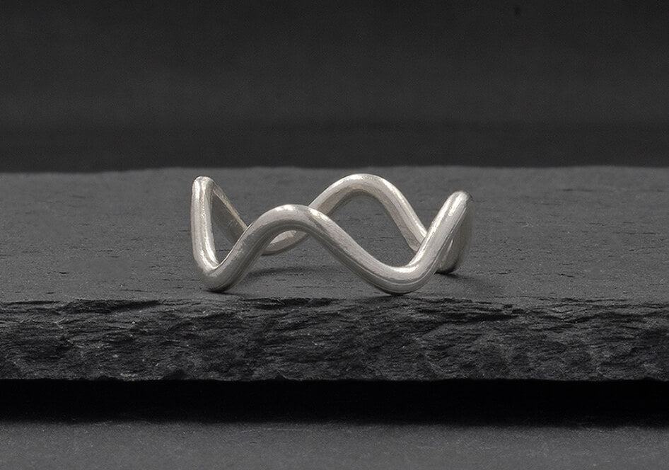 Minimalist wave ring from Hill to Street seating on a dark grey stone over black background