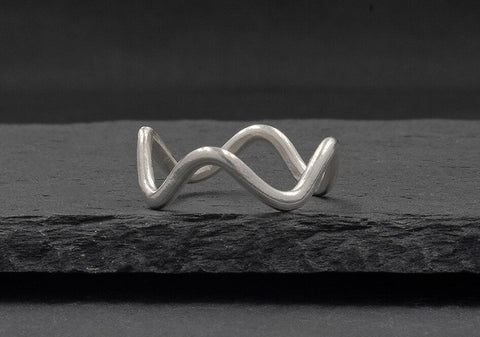 Minimalist wave ring from Hill to Street seating on a dark grey stone over black background